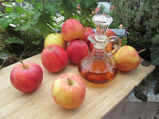 Färska äpplen och en flaska äppelcidervinäger på bordet.