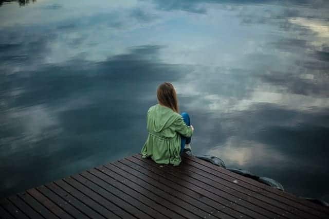  en kvinna sitter på kanten av en brygga och tittar ut i vattnet