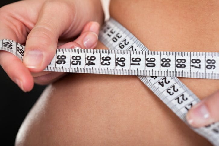  en kvinna mäter sin midja med en centimeter