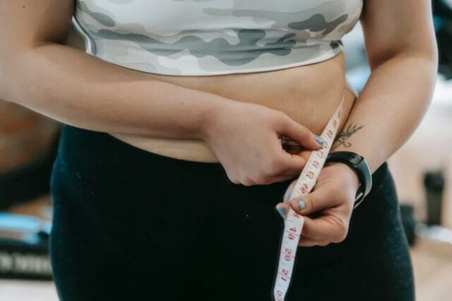  En överviktig kvinna mäter sin midja med en centimeter.