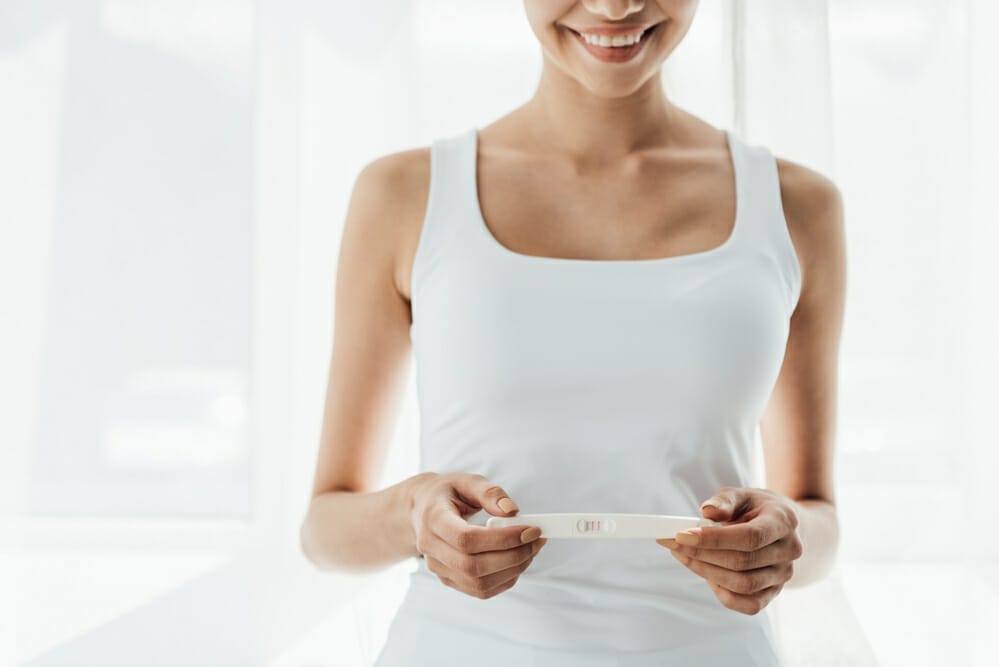 en nöjd kvinna håller ett positivt graviditetstest i handen